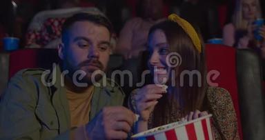 在电影院看电影时，一对夫妇吃爆米花，互相喂饭。 年轻的男人和女人